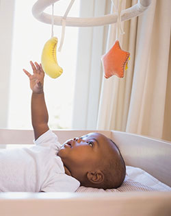 BABY REACHING UP TO TOY IN COT